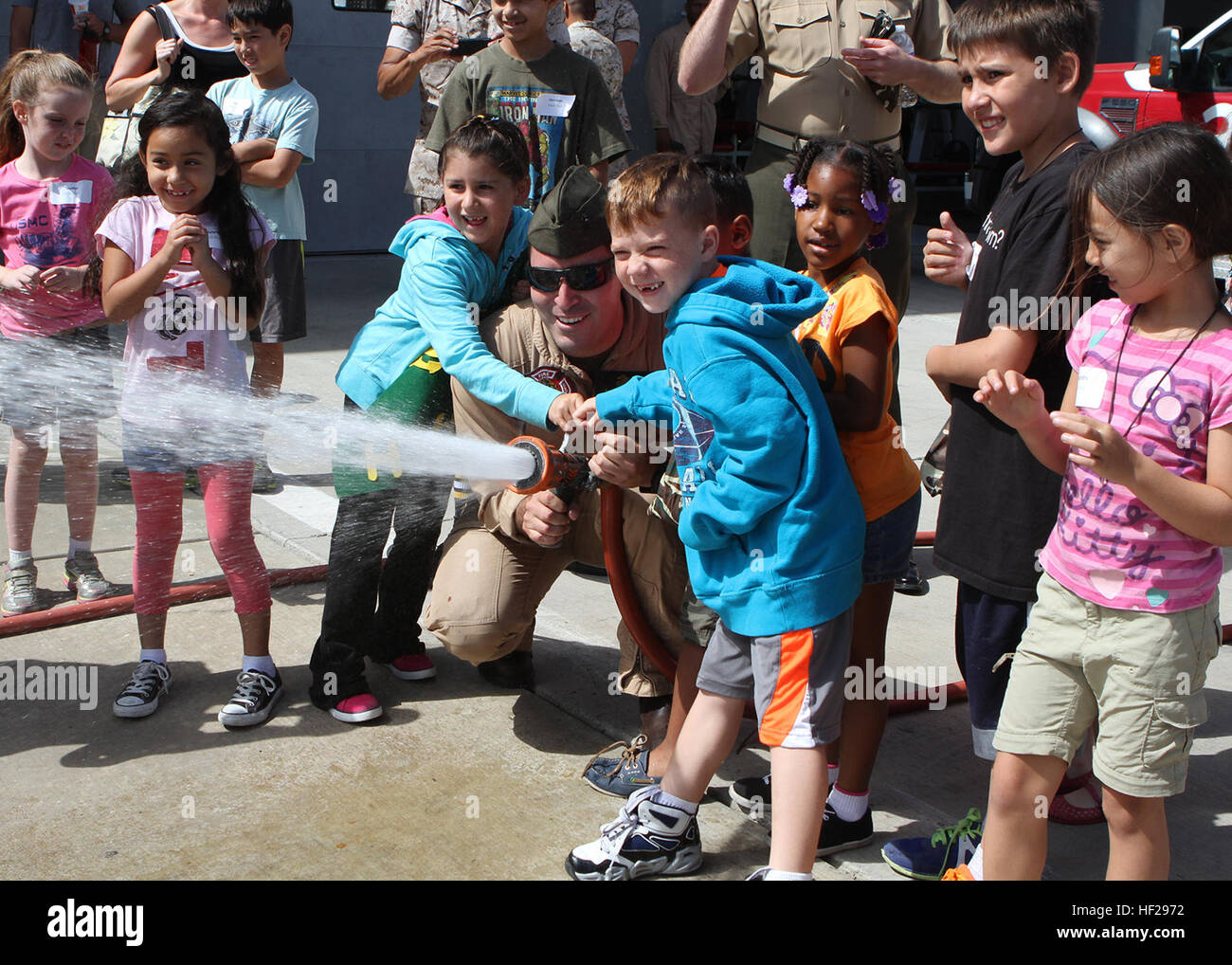 Cpl. Andrew Martinez, a crew chief with Aircraft Rescue and Firefighting, helps children operate a fire hose during a Lil' Leatherneck day aboard Marine Corps Air Station Miramar, Calif., June 27. The Headquarters and Headquarters Squadron event served as an interactive tool for children to gain understanding about their parents' military life. LilE28099 Leathernecks learn about military lifestyle 140627-M-YG675-178 Stock Photo