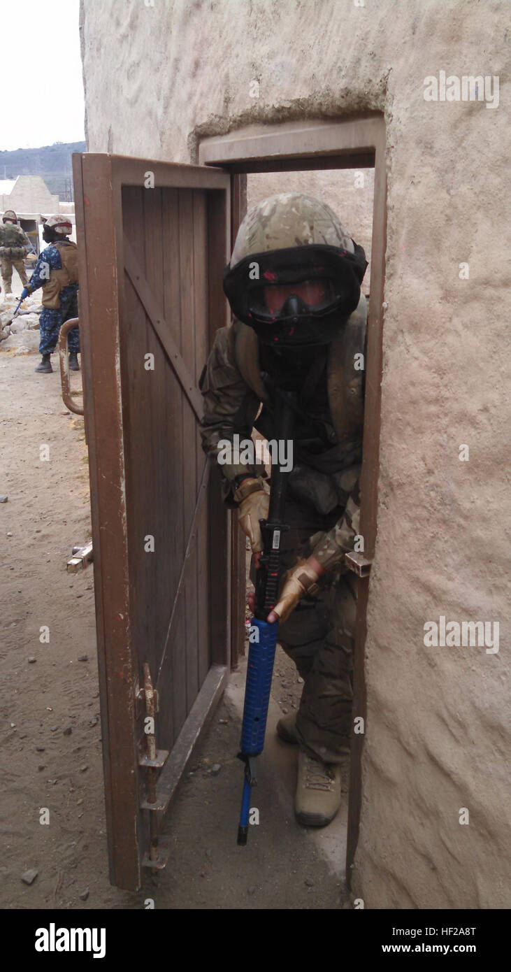 A British Army commando peeks through a doorway to clear an alley ...