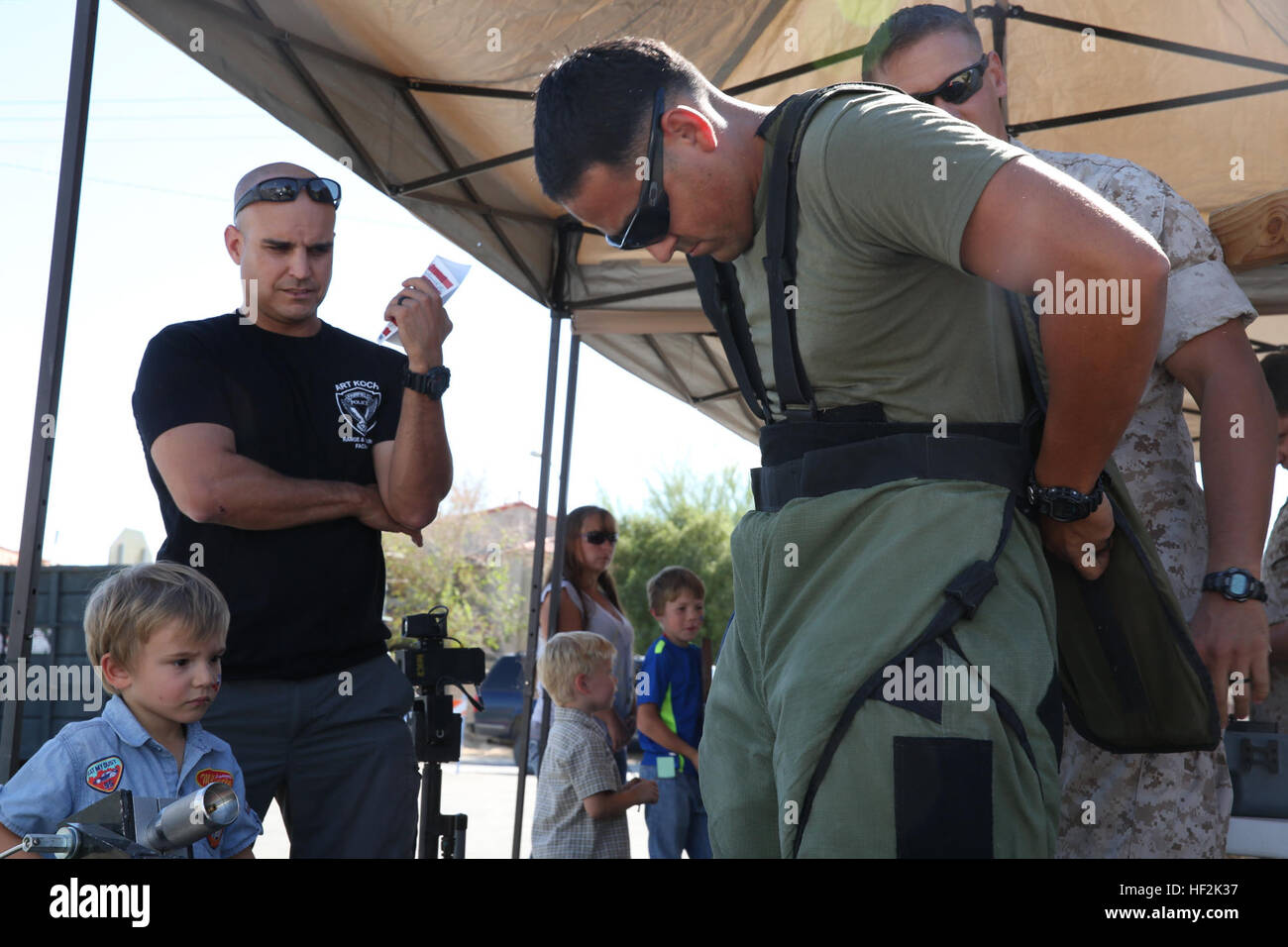 Sgt. Oscar Morales, explosive ordnance technician, Combat Center Explosive Ordnance Disposal team, demonstrates how to put on the EOD suit for Urijah Andress and his father, Capt. Adam Andress, during the Pioneer Days Fair at Luckie Park, Twentynine Palms, Calif., Oct. 19, 2014. The EOD team showed people at the fair some of the gear used when defusing explosives. (Official Marine Corps photo by Pfc. Julio McGraw/ Released) Combat Center Marines participate in Pioneer Days 141019-M-TM495-705 Stock Photo