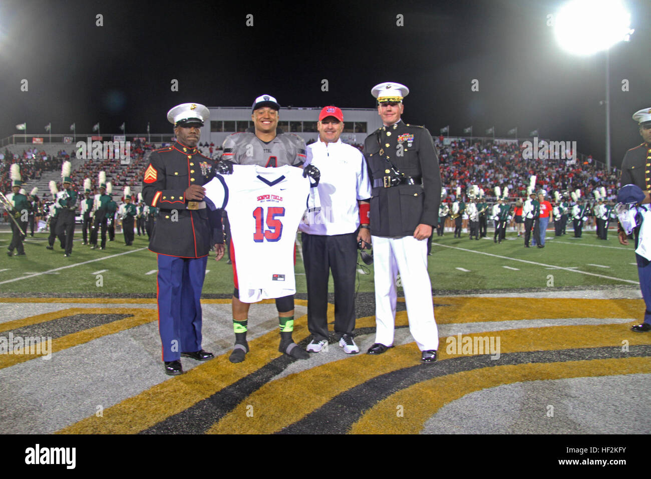 Richard Moore, a linebacker from Cedar Hill High School selected to play in the 2015 Semper Fidelis All-American Bowl, alongside Joey McGuire, Cedar Hill High School Head Football Coach, receives his jersey from Maj. Charles Nicol (right), the commanding officer of Recruiting Station Dallas, and Sgt. Timothy Clark (left), a recruiter with Recruiting Substation Dallas South, during the halftime ceremony of the Desoto vs. Cedar Hill High School football game Oct. 23. The United States Marine Corps is recognizing exemplary student athletes across the country through the Semper Fi Bowl. Now in its Stock Photo