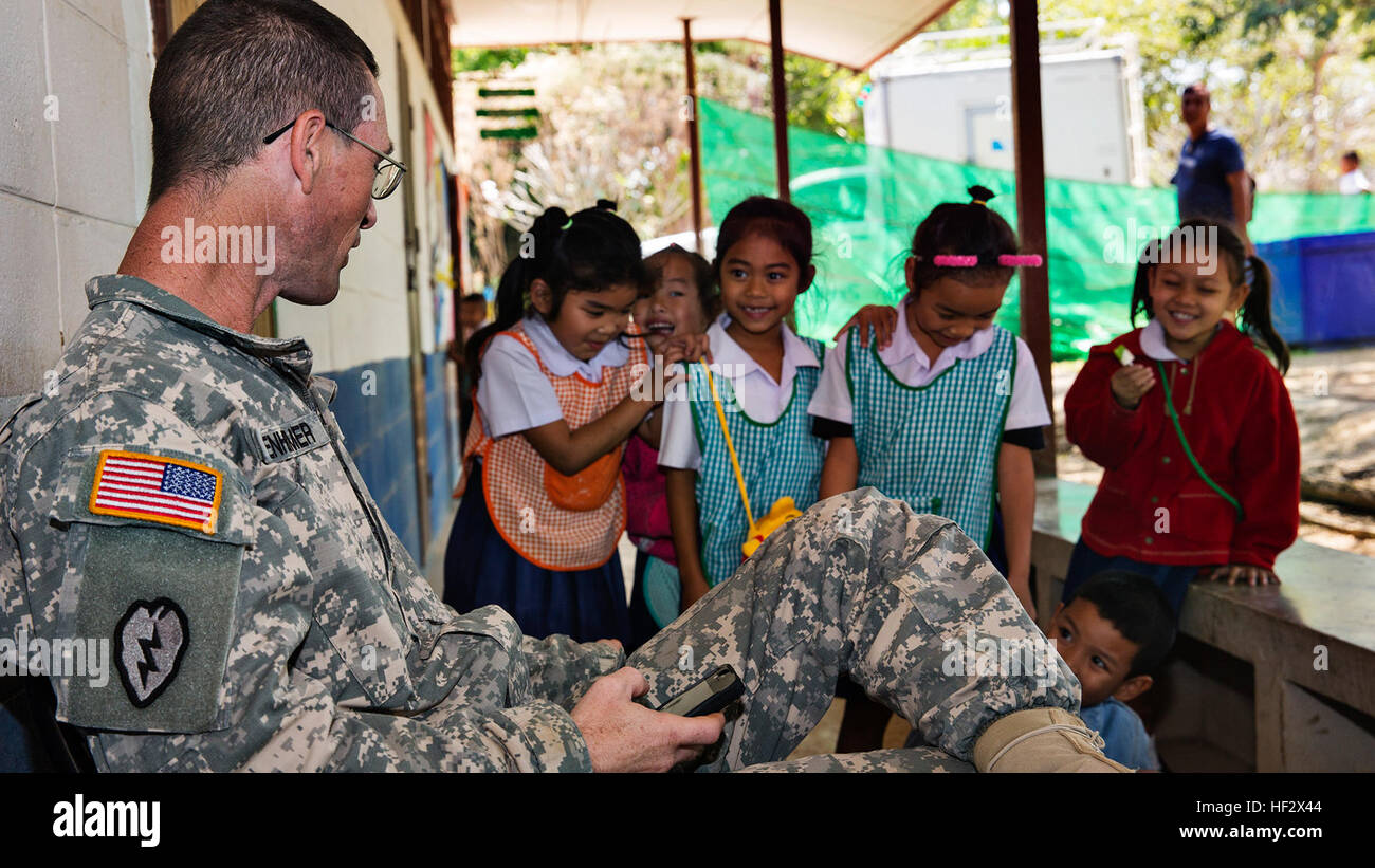 U.S. Army Sgt. 1st Class Michael Gegenheimer, the platoon sergeant for a detachment of soldiers participating in Exercise Cobra Gold 2015 from Washington National Guard’s 176th Engineering Company (Vertical), based out of Snohomish, Wash., talks to Thai children at Ban Sub Prik Elementary School, located in Muak Lek District, Saraburi Province, Thailand, on Feb. 6, 2015. As part of CG15, a combined force of U.S. Army, Royal Thai Air Force and Indonesian Marine Corps vertical engineers are constructing a new multipurpose facility at Ban Sub Prik Elementary School. The facility will serve as a c Stock Photo