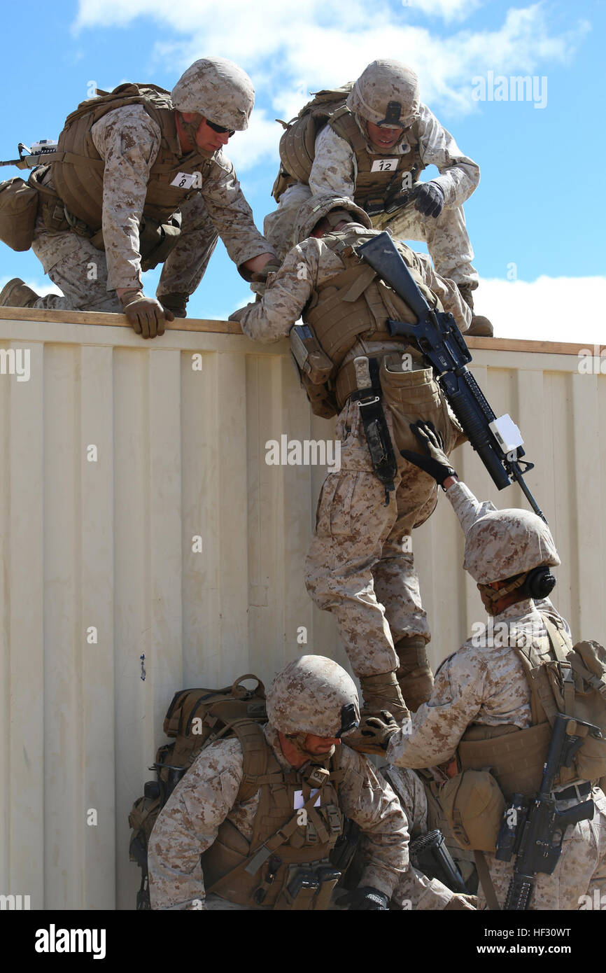 Marines with Company A, Ground Combat Element Integrated Task Force, assist each other in climbing over an eight-foot wall obstacle during a pilot test at Range 107, Marine Corps Air Ground Combat Center Twentynine Palms, California, March 2, 2015, in preparation for the Marine Corps Operational Test and Evaluation Activity assessment. From October 2014 to July 2015, the GCEITF will conduct individual and collective level skills training in designated ground combat arms occupational specialties in order to facilitate the standards-based assessment of the physical performance of Marines in a si Stock Photo