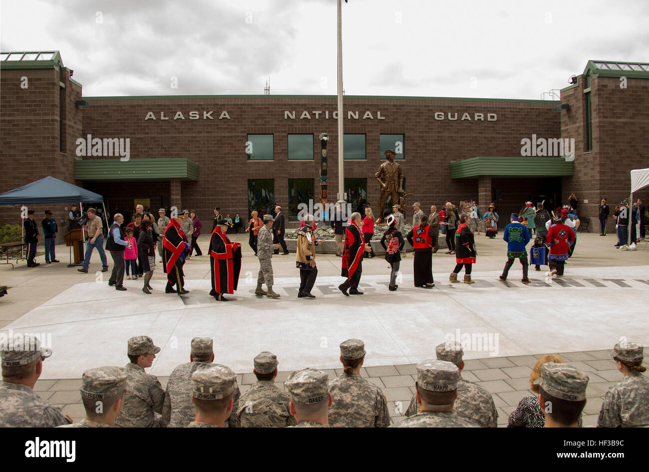 Gov. Bill Walker, center in red and black Tlingit button blanket, and Lt. Gov. Byron Mallott, left of governor, participate in a Blessing and Cleansing ceremony at the Alaska National Guard armory on Joint Base Elmendorf-Richardson May 26. The Blessing and Cleansing ceremony is a complex and symbolic event to reinvigorate the spirit of the National Guard that is embodied in the honor pole, which was carved by George Bennett and his son James Bennett in Sitka, Alaska, to honor the Alaska National Guard’s past and present military service, seen in the background. Alaska National Guard receives n Stock Photo