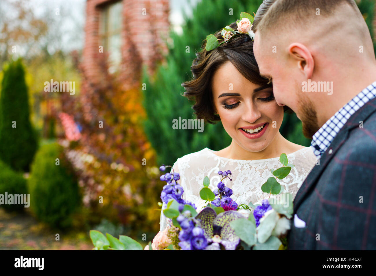 Portrait of emotional newlyweds groom and bride embracing  holding each other hands. In yard against house in autumn season. Stock Photo