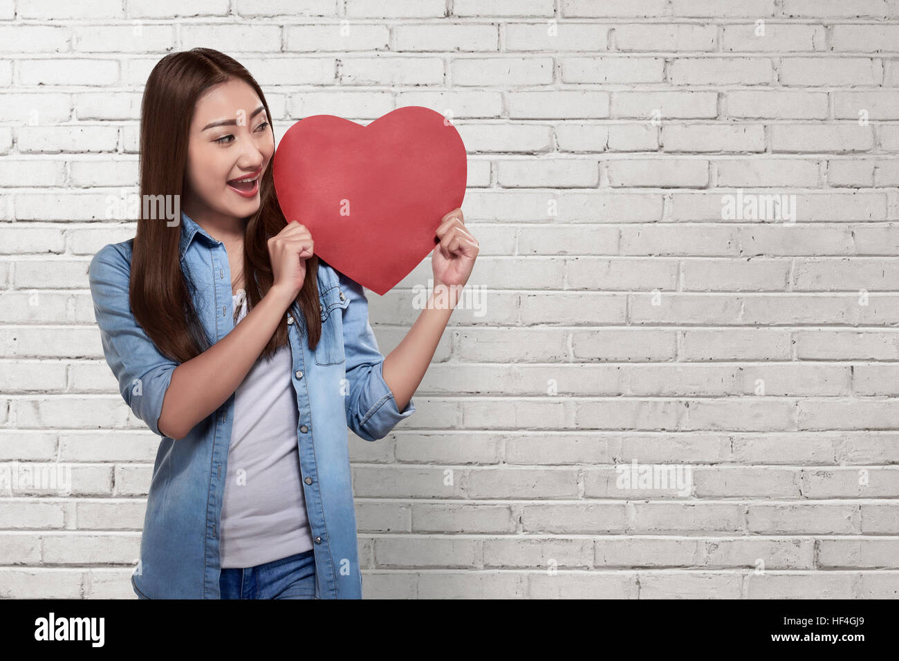 Beautiful asian woman holding red heart over white brick wall ...