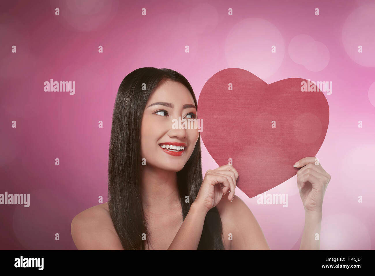 Young asian woman smiling with holding red heart over pink background ...