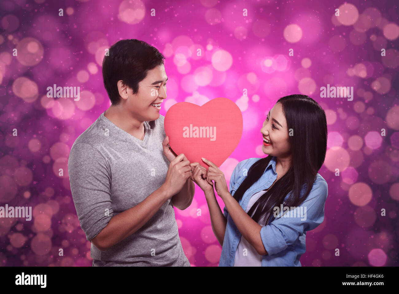 Happy asian couple standing holding red heart against blurred light ...