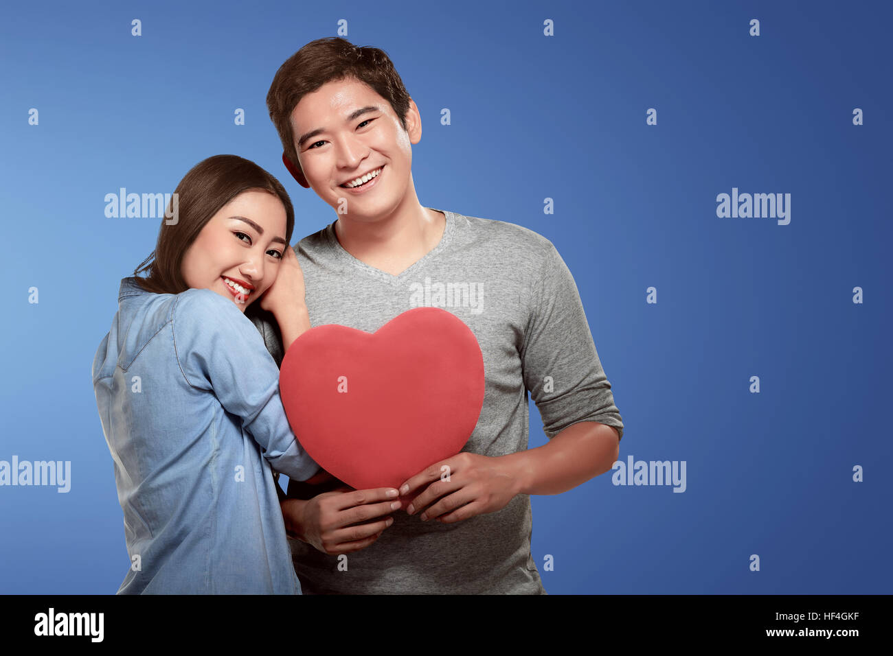 Happy asian couple leaning and holding heart shape over blue background ...