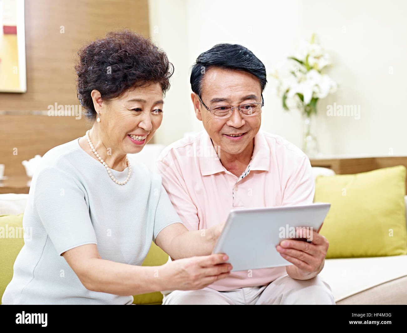 senior asian couple sitting on couch looking at tablet computer together, happy and smiling Stock Photo