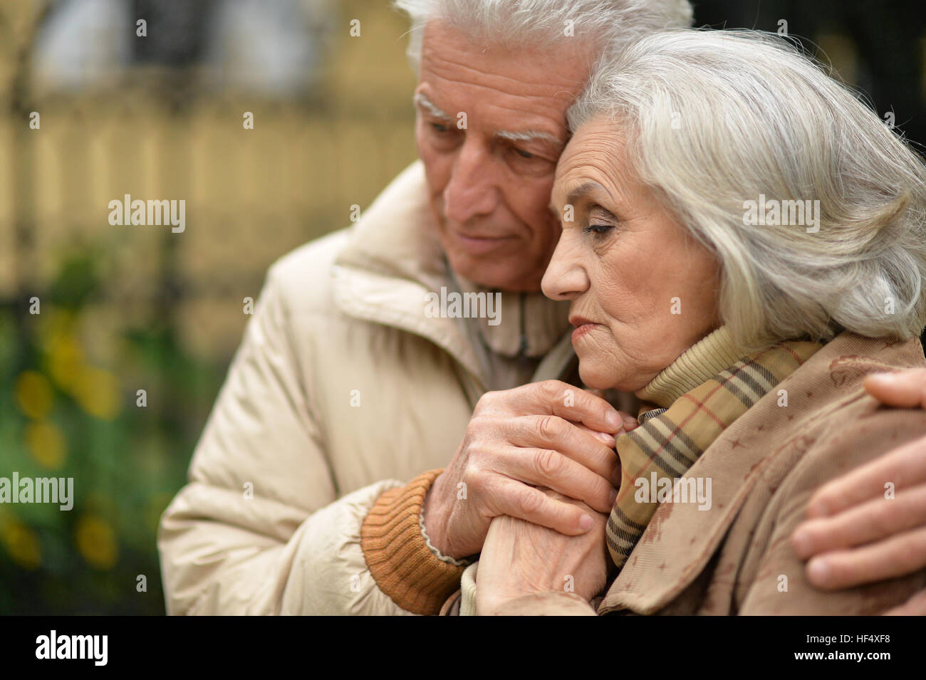 Sad elderly couple standing embracing outdoors Stock Photo