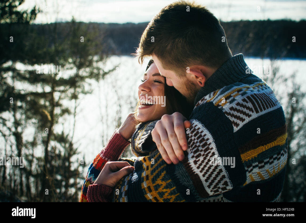 Joyful cute couple embraces. Young man in a sweater hugs a girl from behind background in winter. Stock Photo