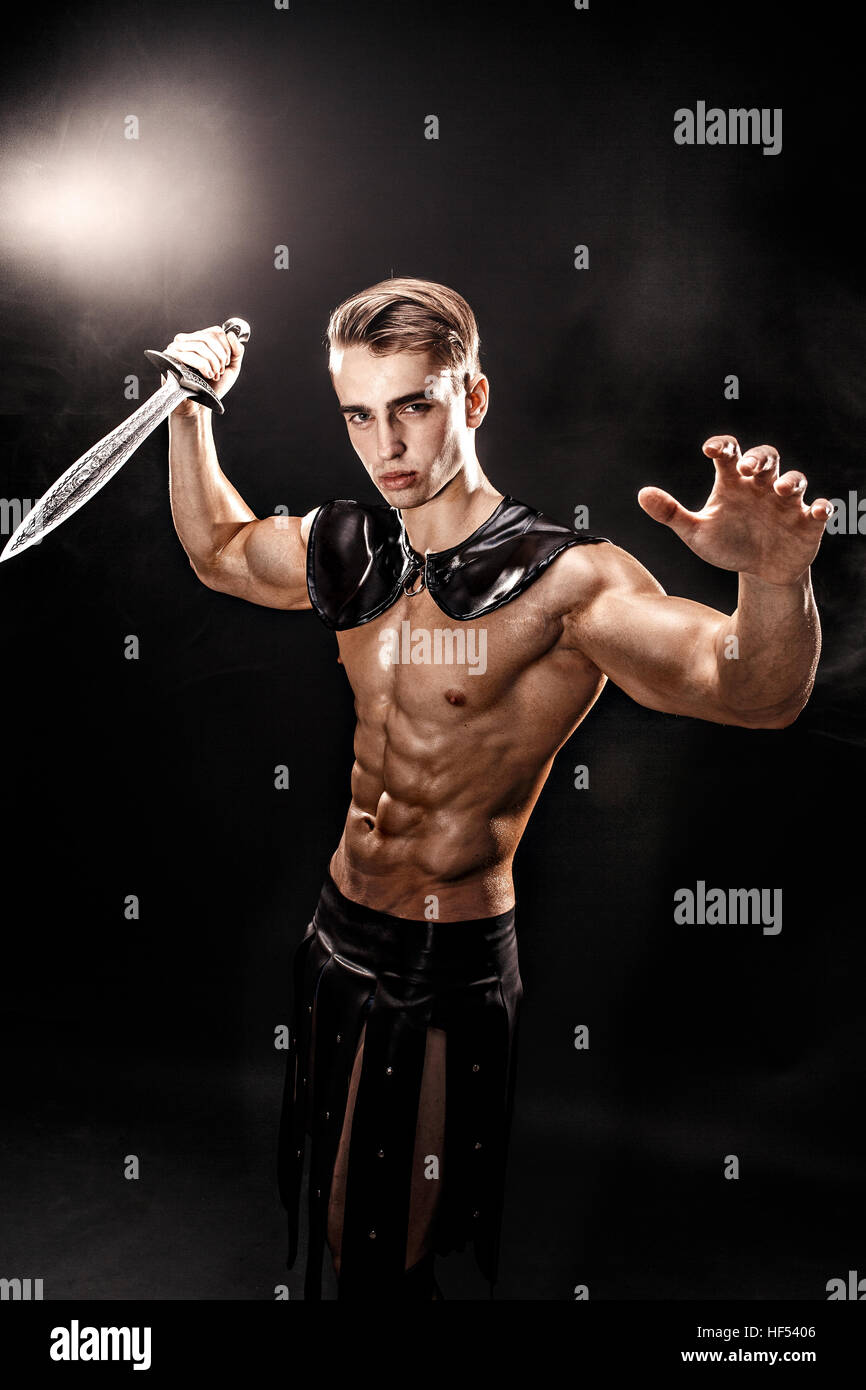 Portrait of handsome muscular gladiator with sword. Isolated. Studio shot. Black background Stock Photo