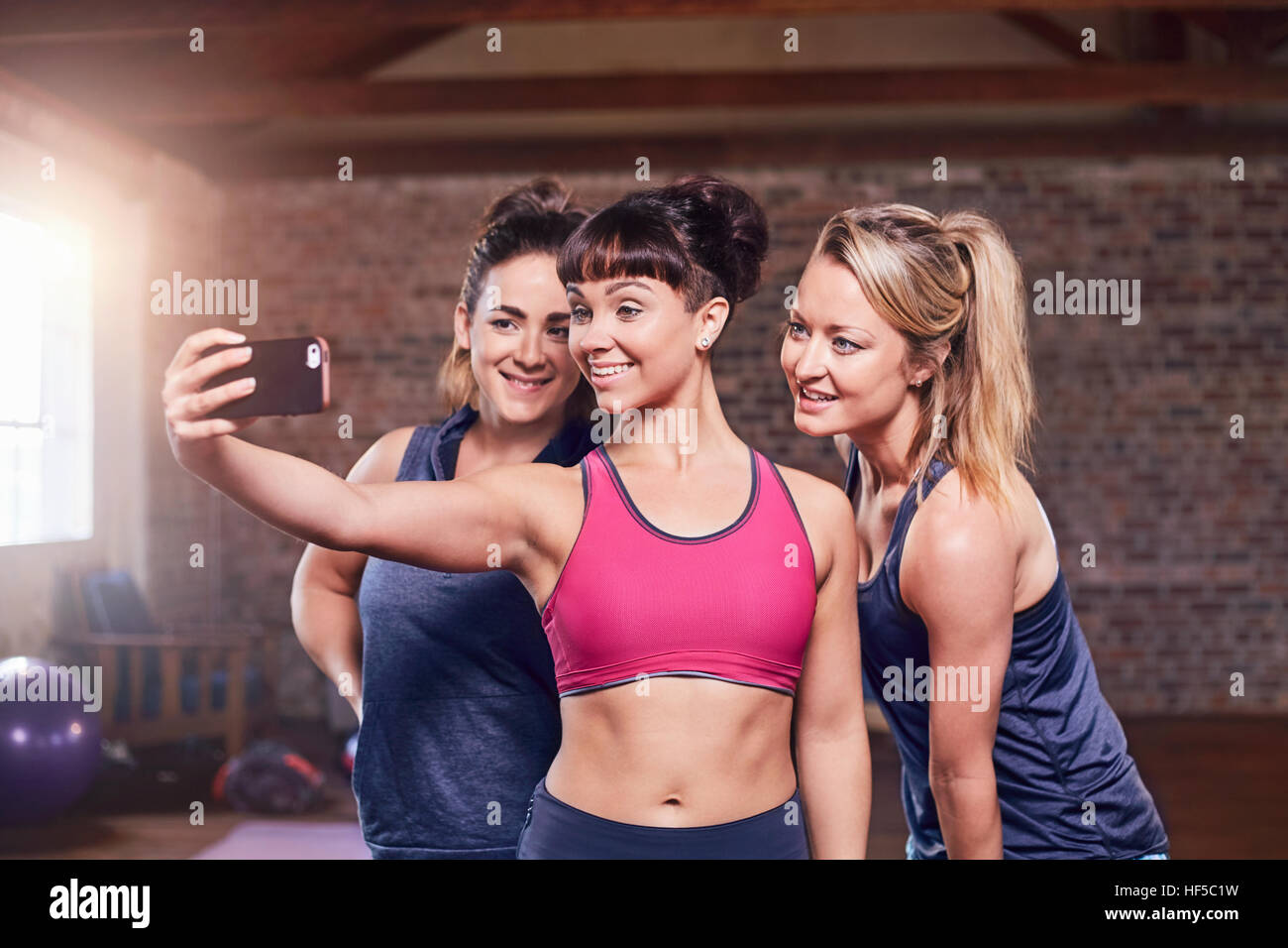 Fit young women in sports clothing taking selfie with camera phone in gym studio Stock Photo
