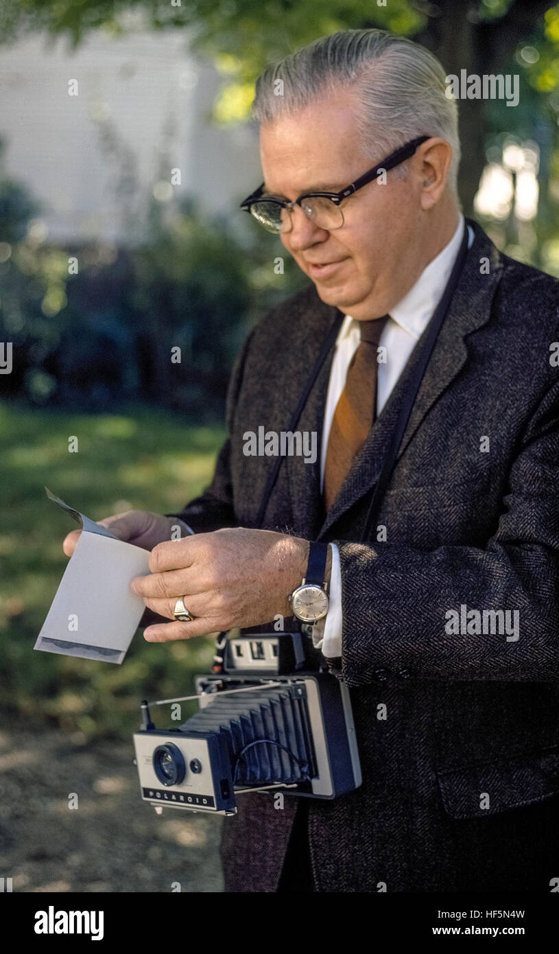 A man peels the chemical backing away from an 'instant' photographic print that was created with an early model of the Polaroid Land camera. Introduced in 1947 by its inventor, Dr. Edwin Land, the novel Polaroid camera produced a black-and-white snapshot picture only a few seconds after the exposure was made. The peel-apart Polaroid film was pulled from the camera by the photographer, who then had to separate the print from its chemical-covered negative. Later Polaroid films turned into finished color photographs that were automatically ejected by the camera after a picture was taken. Stock Photo
