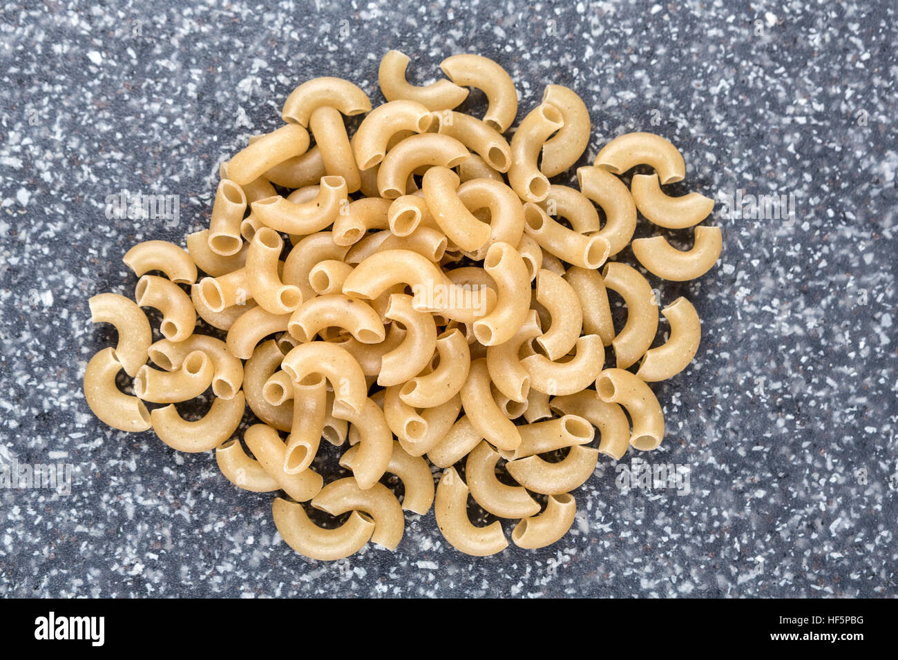 Brown rice elbow macaroni on a mottled grey blue background Stock Photo