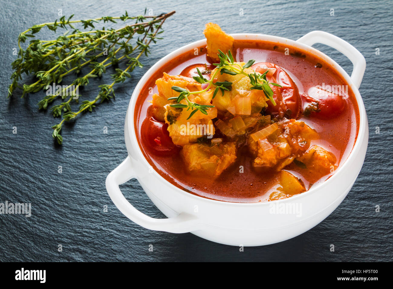 Fish soup with cod, tomato, onion, garlic and thyme in white bowl on