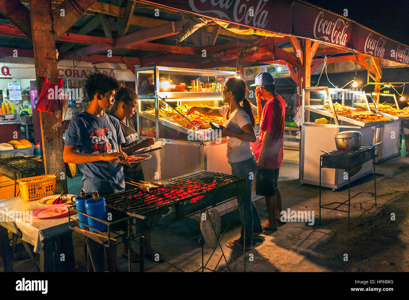 Customers at the night seaside barbecue stand buy skewers of variety