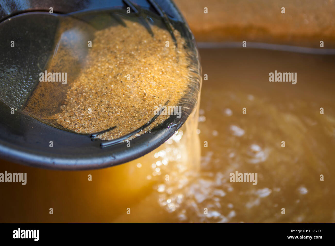 Close up of gold panning pan with sifting sand. Shallow depth of field with focus on sand flowing over edge of pan into water. Stock Photo