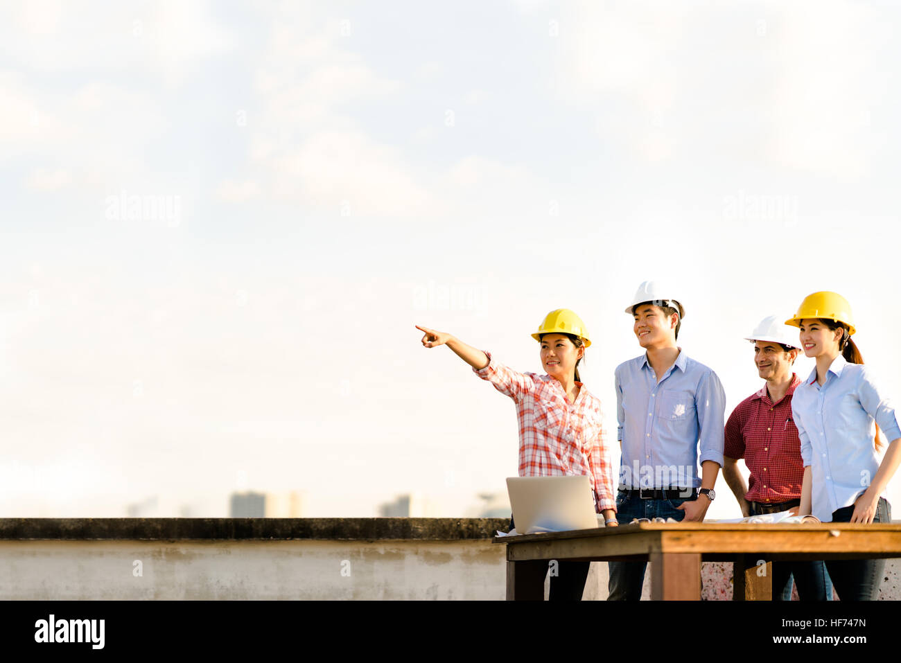 Multiethnic diverse group of engineers or business partners at construction site, pointing toward copy space on sky during sunset, engineering industr Stock Photo