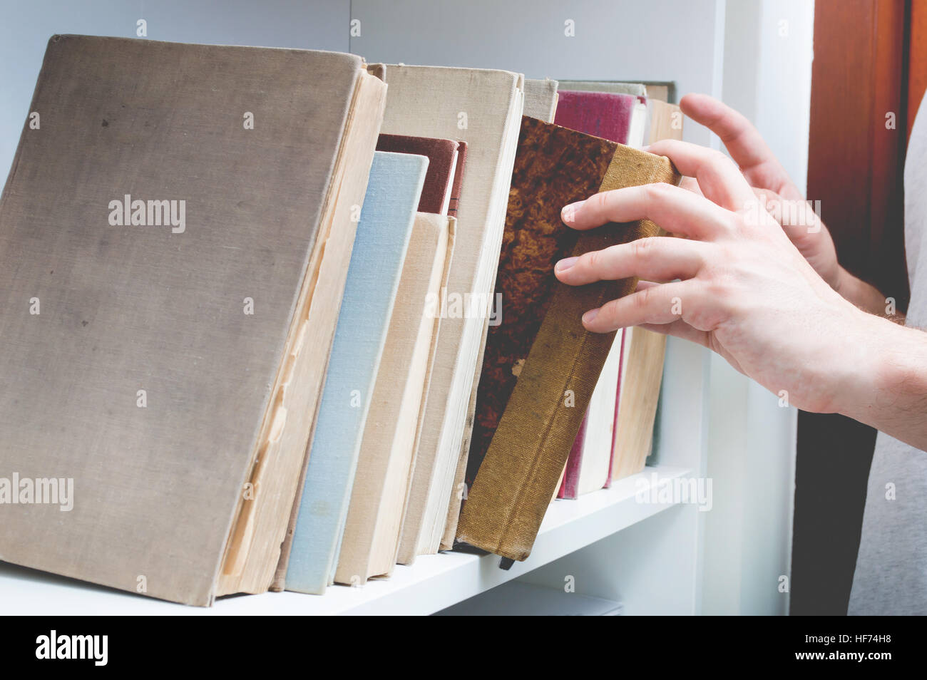 Man chose book from bookshelf. Image performed in vintage stylization. Stock Photo