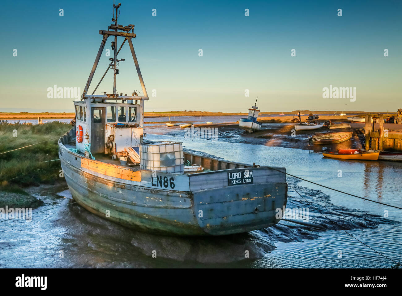 A commercial fishing boat at low tide in a staithe on a  coastal estuary Stock Photo