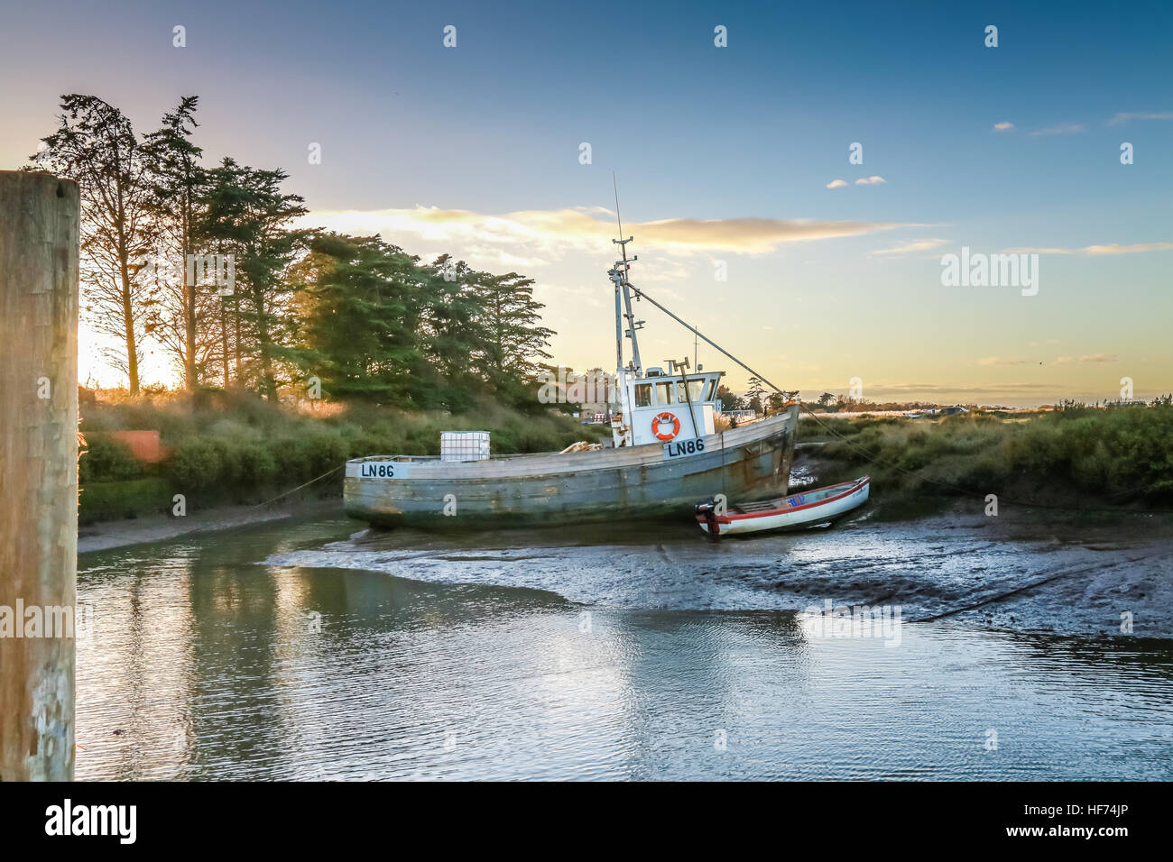 A commercial fishing boat at low tide in a staithe on a  coastal estuary Stock Photo