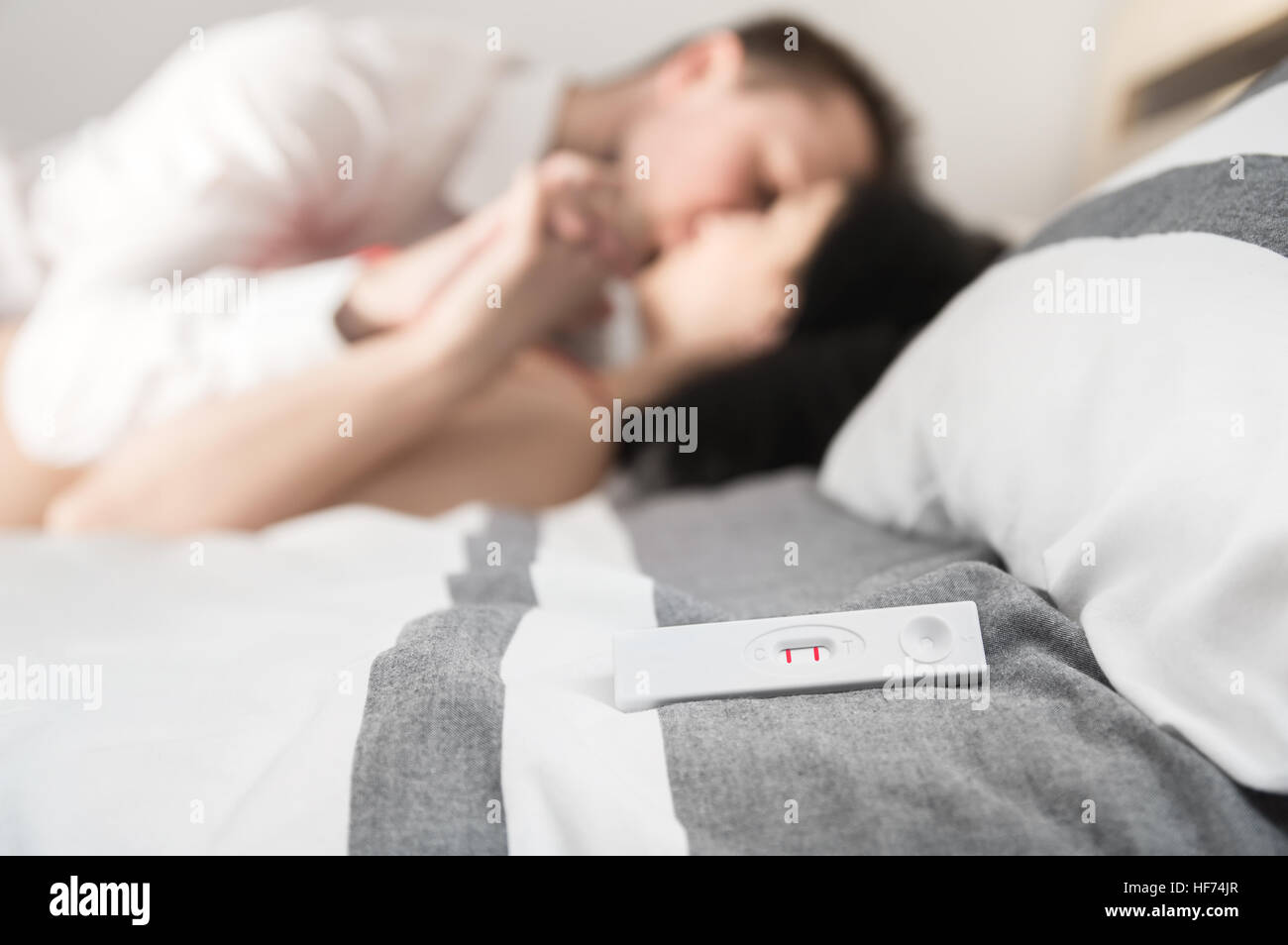 Positive pregnancy test is laying on the bed. Happy couple enjoyed on background Stock Photo