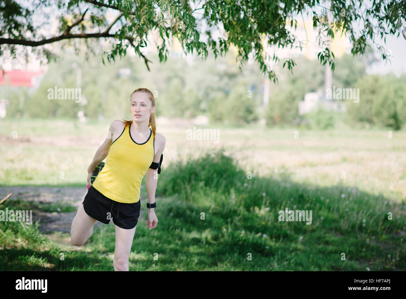 Young fitness woman stretching body before run. Sportsman standing under tree. Stock Photo