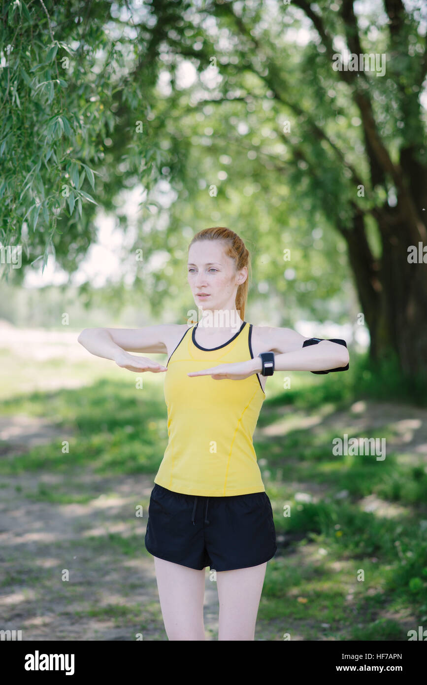 Young fitness woman doing exercise before run. Sportsman standing under tree. Stock Photo