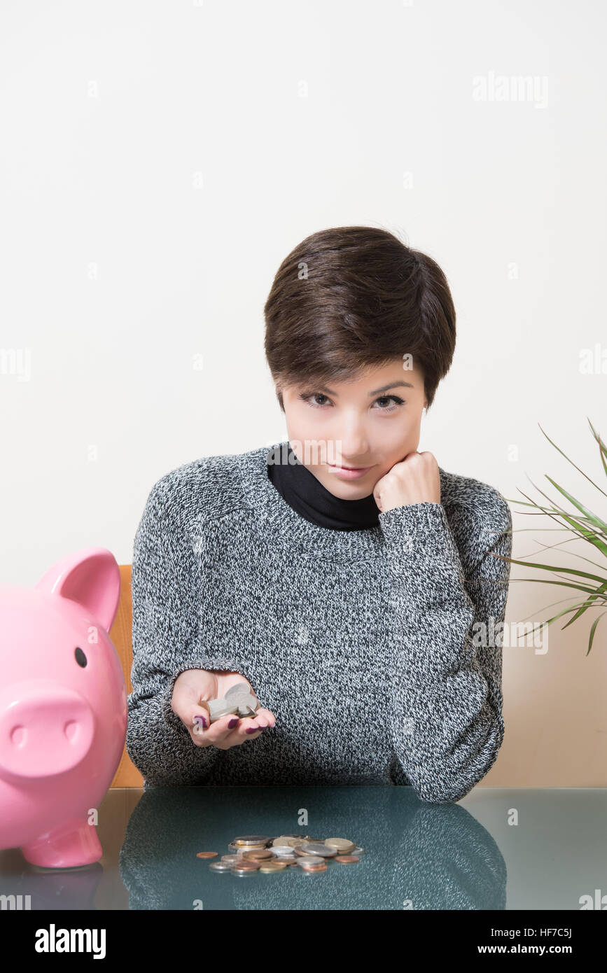 Young woman smiling about savings, coins in the hand and pink piggy bank on desktop Stock Photo