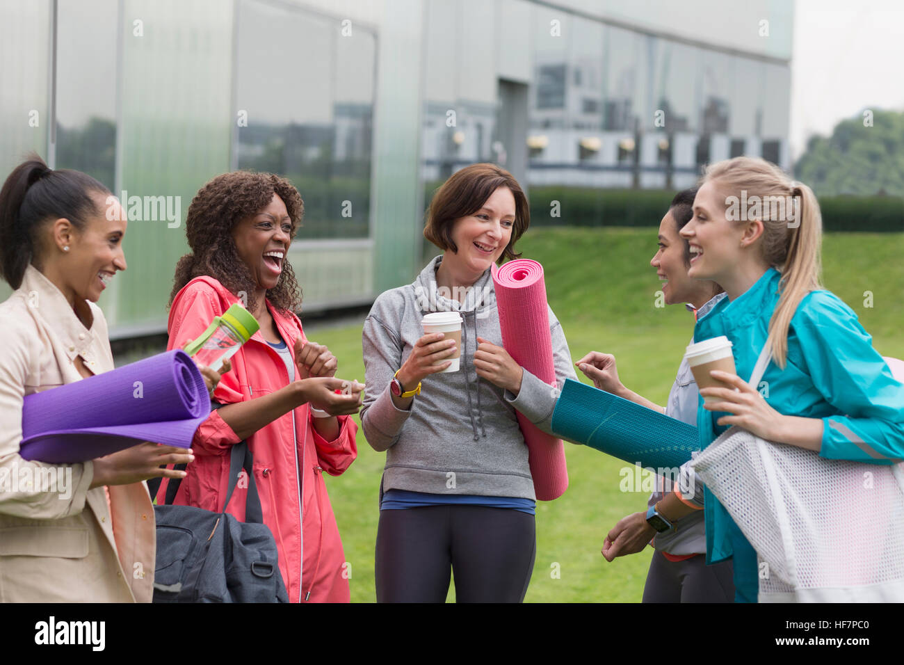 Women friends with yoga mats and coffee talking outside gym Stock Photo