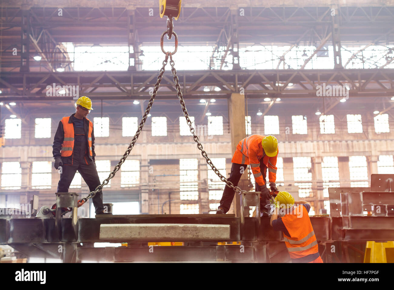 Steel workers fastening crane chain in factory Stock Photo