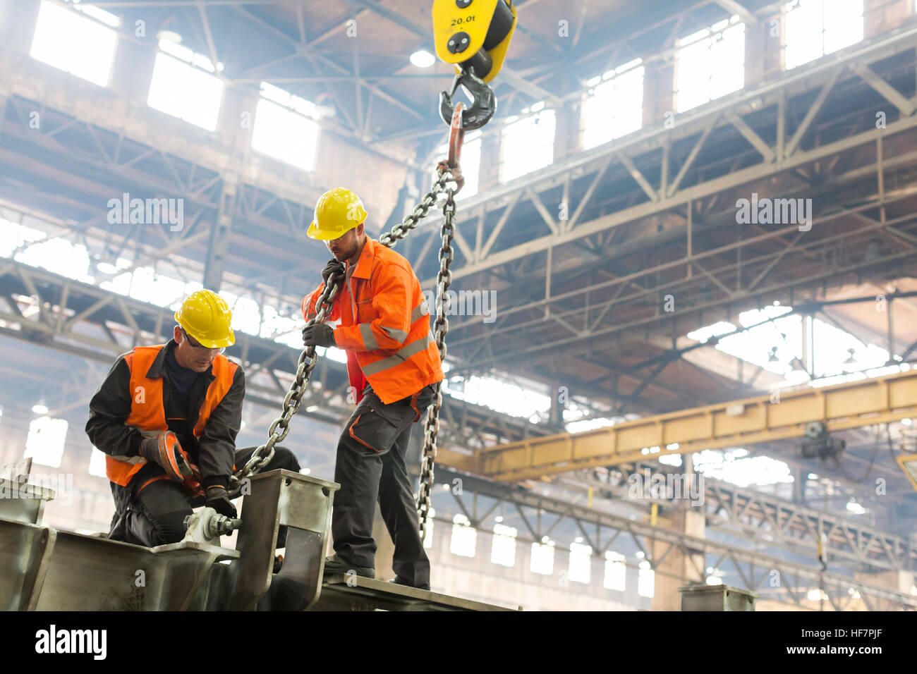 Steel workers fastening crane chain to steel in factory Stock Photo