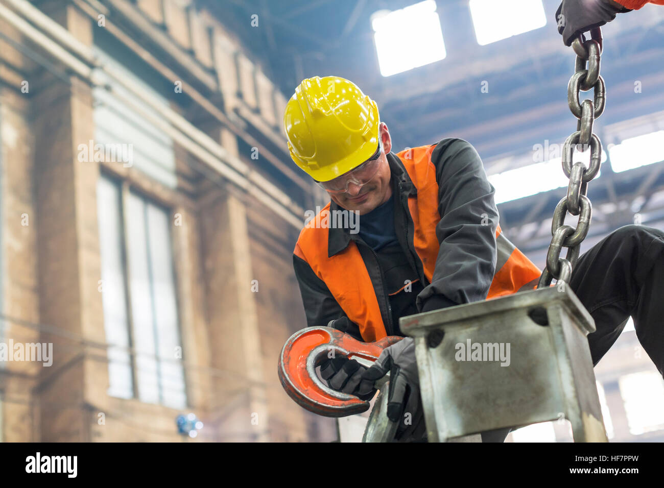 Steel worker fastening crane chain to steel in factory Stock Photo