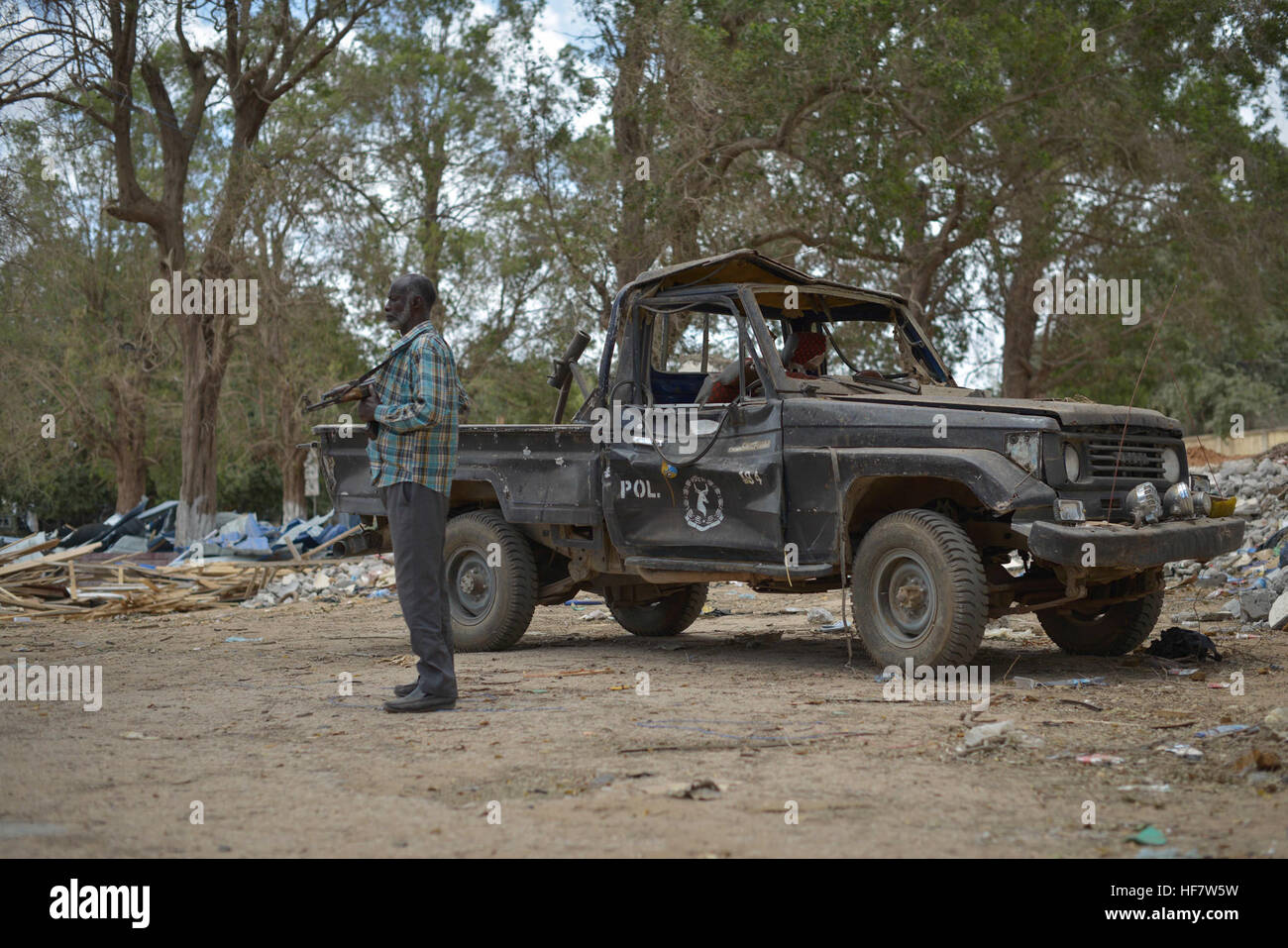 A Somali Police Force officer stands next to a vehicle damaged in a bomb blast at a police station in Afgoye on October 25, 2016. The blast, which occurred the previous week, highlights the ongoing security threats in the region. AU UN IST Photo / Tobin Jones Stock Photo