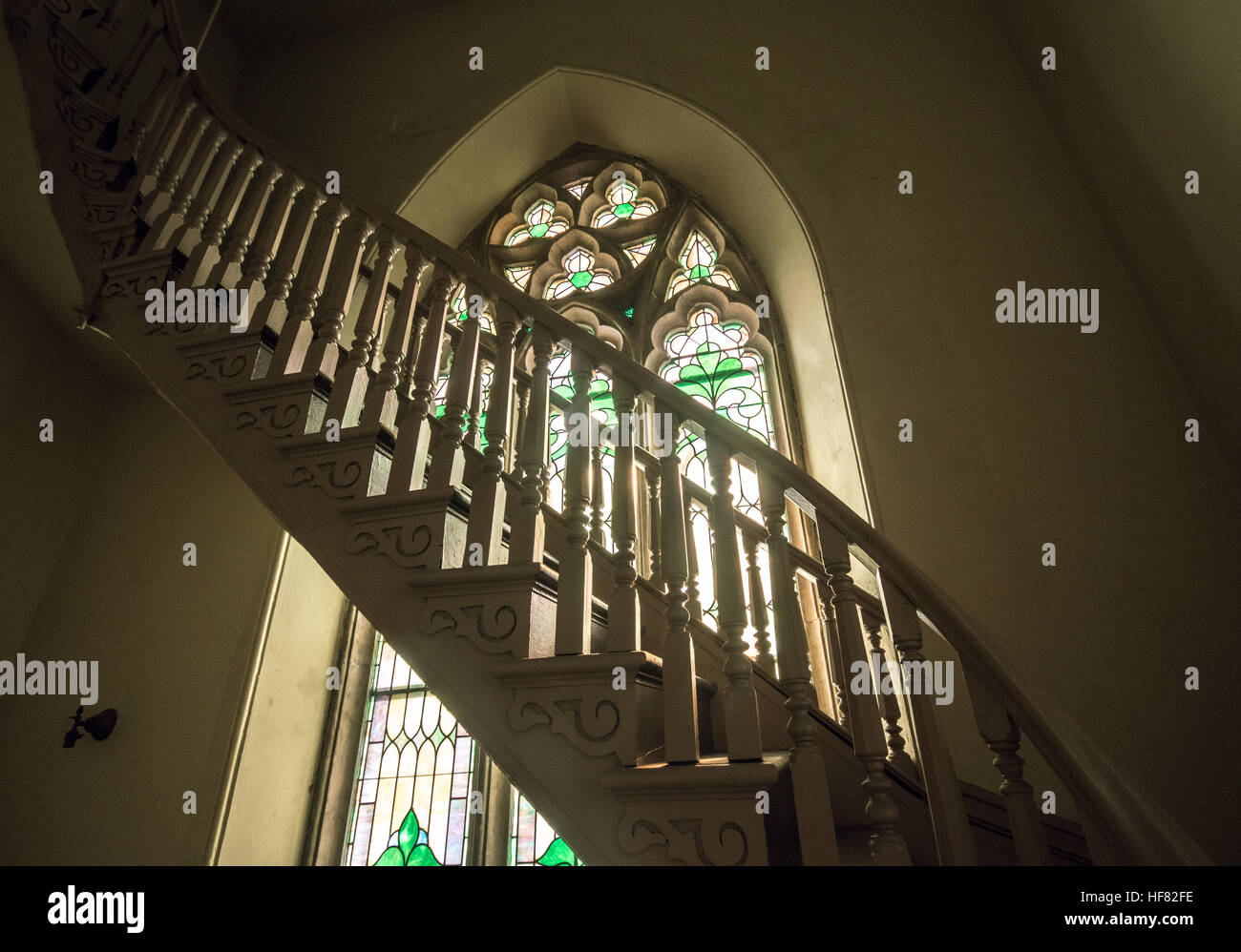 Wooden stairwell ascending in front of a neo-Gothic stained glass window Stock Photo