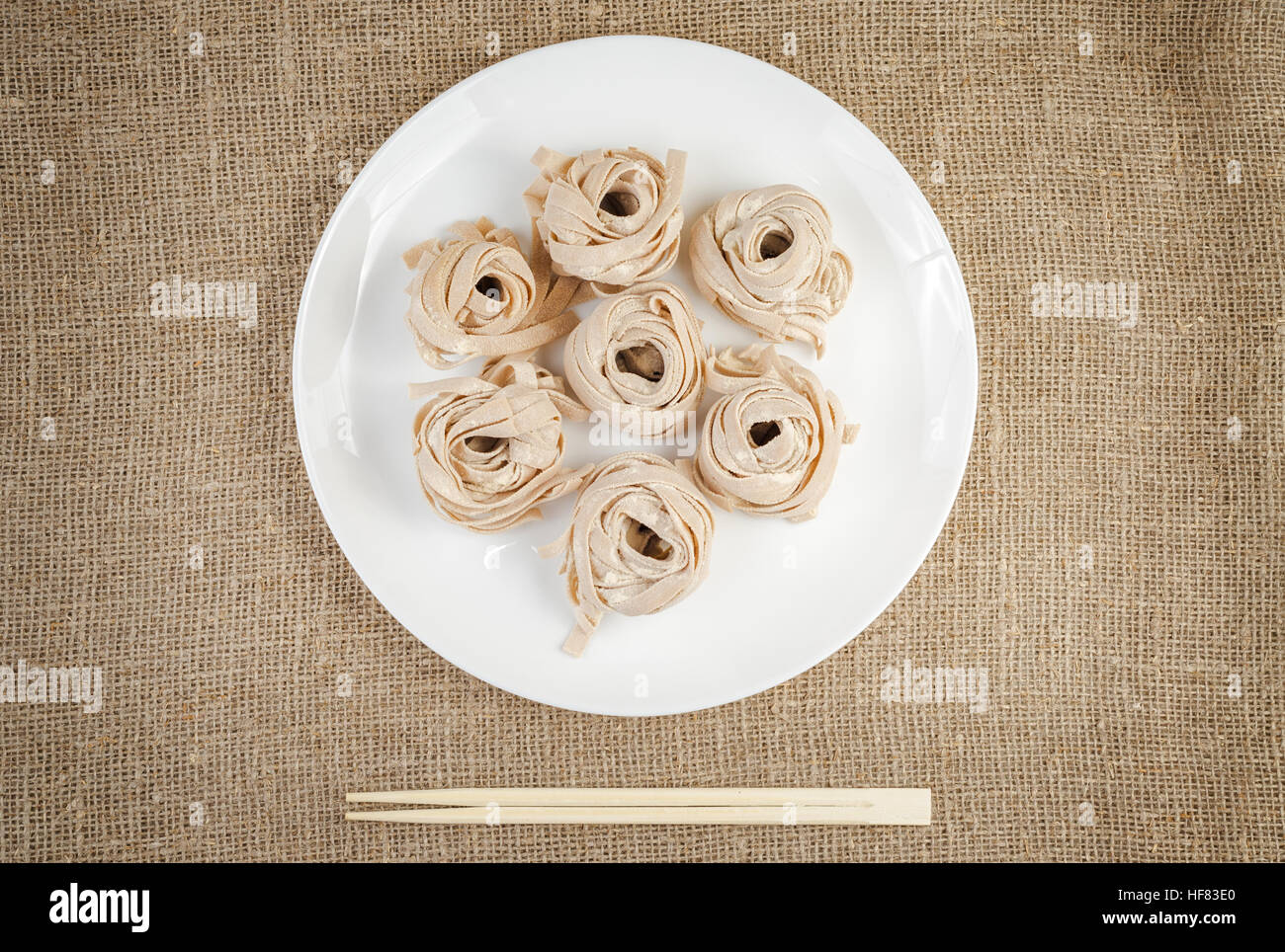 Homemade rolled pasta on linen background with bamboo chopsticks. Portion of raw fettuccine or tagliatelle or pappardelle. Dry pasta from whole wheat Stock Photo