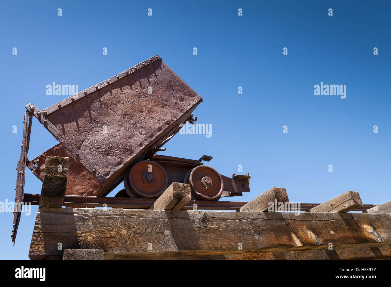 Old rusty mining ore cart on trestle under blue sky. Stock Photo