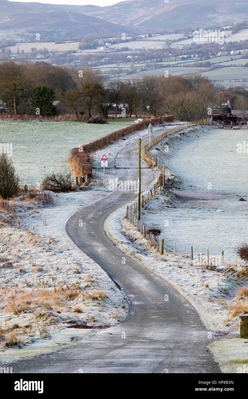 A meandering country lane frozen in rural Flintshire in Wales with the Clwydian Range hills in the distance Stock Photo