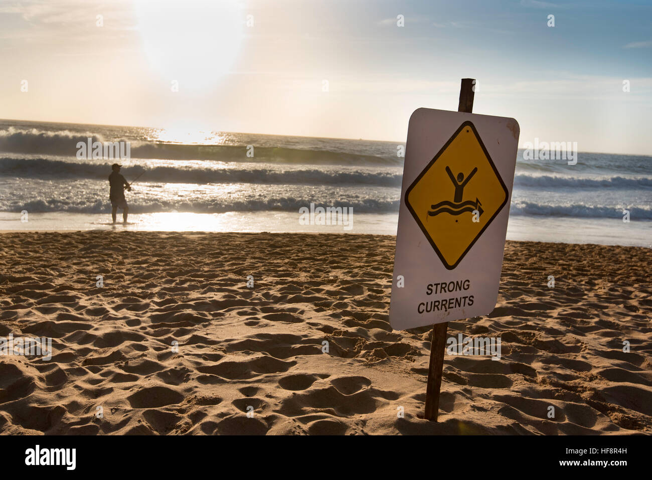 A man fishing and a surf warning sign at a Sydney beach early on a summer morning Stock Photo