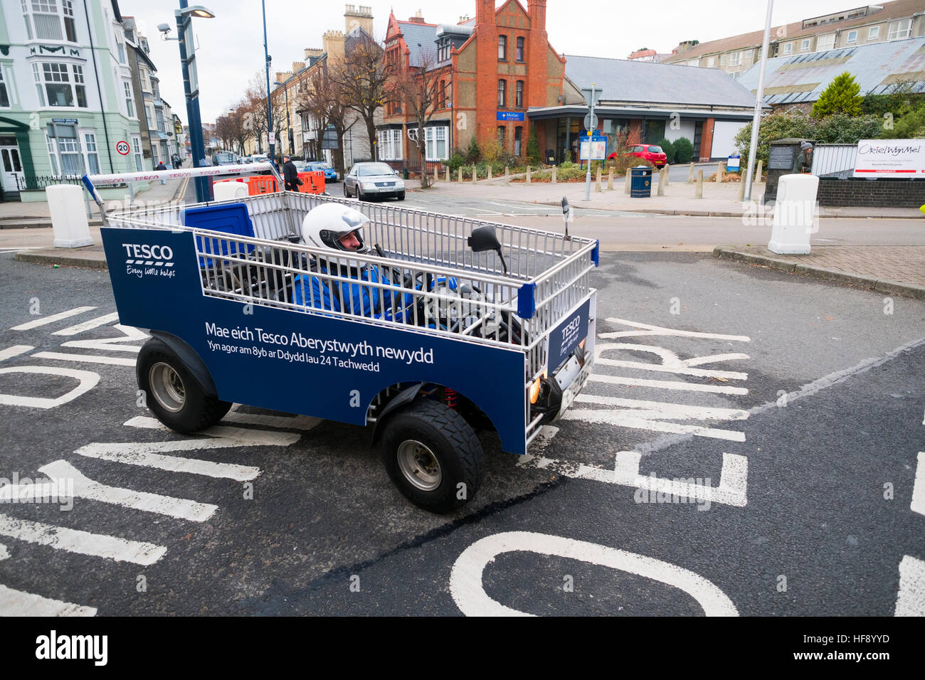 A man driving a motorised shopping trolley on the road in a Tesco promtional stunt to announce the opening of their new supermarket store in Aberystwyth Wales UK Stock Photo