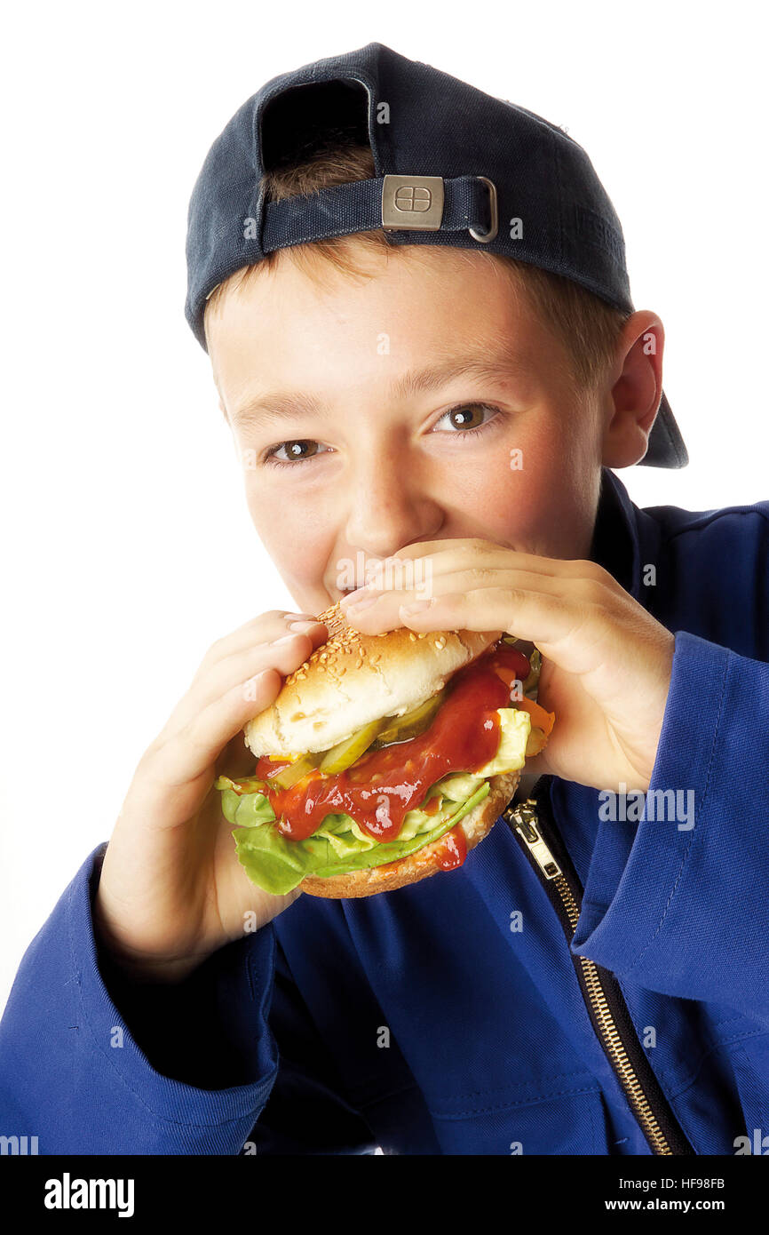 Young boy wearing blue overalls biting into a hamburger Stock Photo