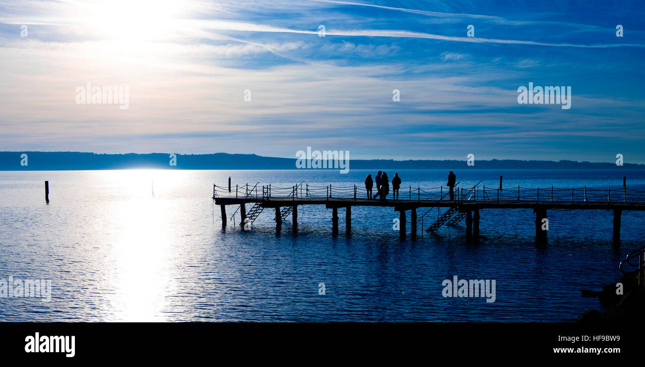 Pier on the sea with people on it, silhouetted against the strong sun Stock Photo