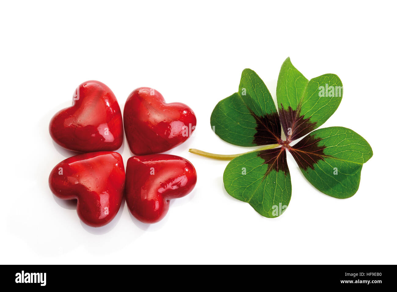Four red hearts formed to resemble a four-leaf clover beside an actual four-leaf clover Stock Photo