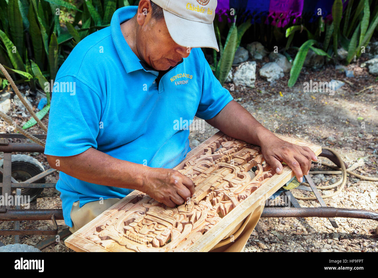 Man hand carving a traditional Mayan scene from wood, to sell at his stall in the grounds of Chichen Itza temple Yucatan, Mexico Stock Photo