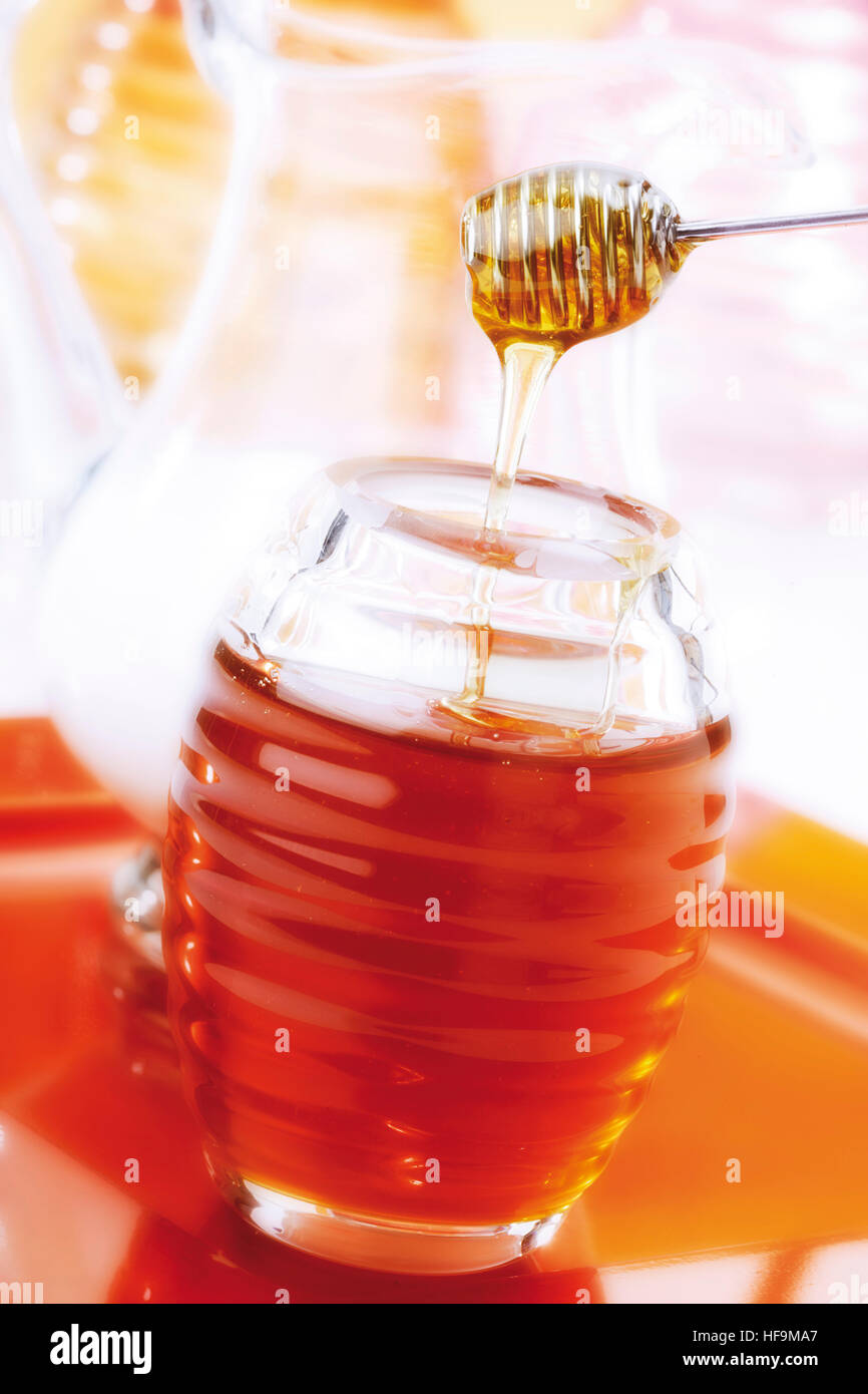 Honey dripping from honey dripper into a jar of honey, jug of milk in ...