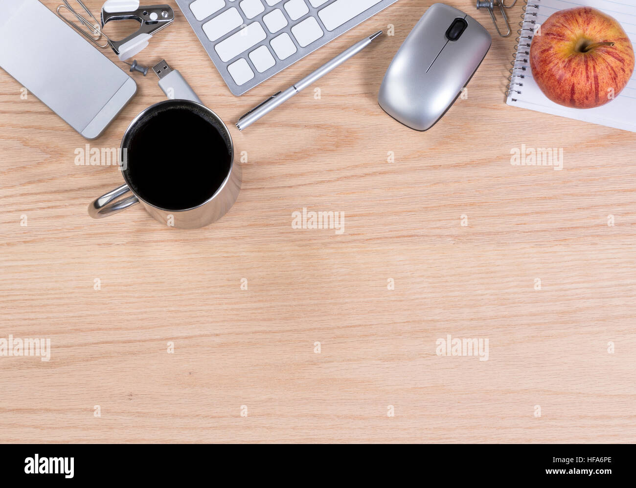 Working office desktop with computer keyboard, mouse, coffee, apple, thumb drive, pen, paper, clip, staple remover, and cell phone. Horizontal format Stock Photo