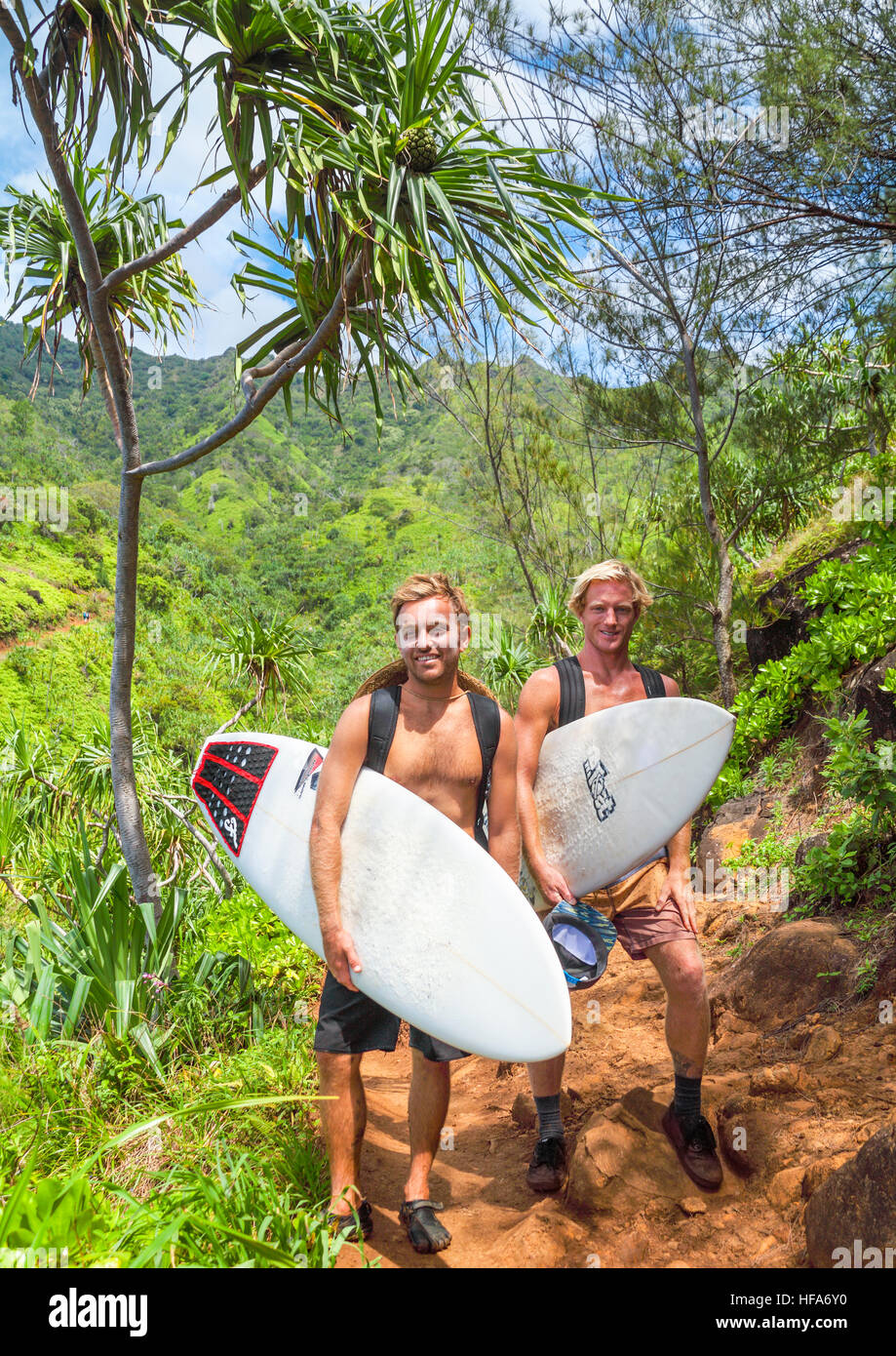 Hikers with surfboards on the rugged Kalalau Trail on Kauai on their way to surf at risky Hanakapiai Beach Stock Photo