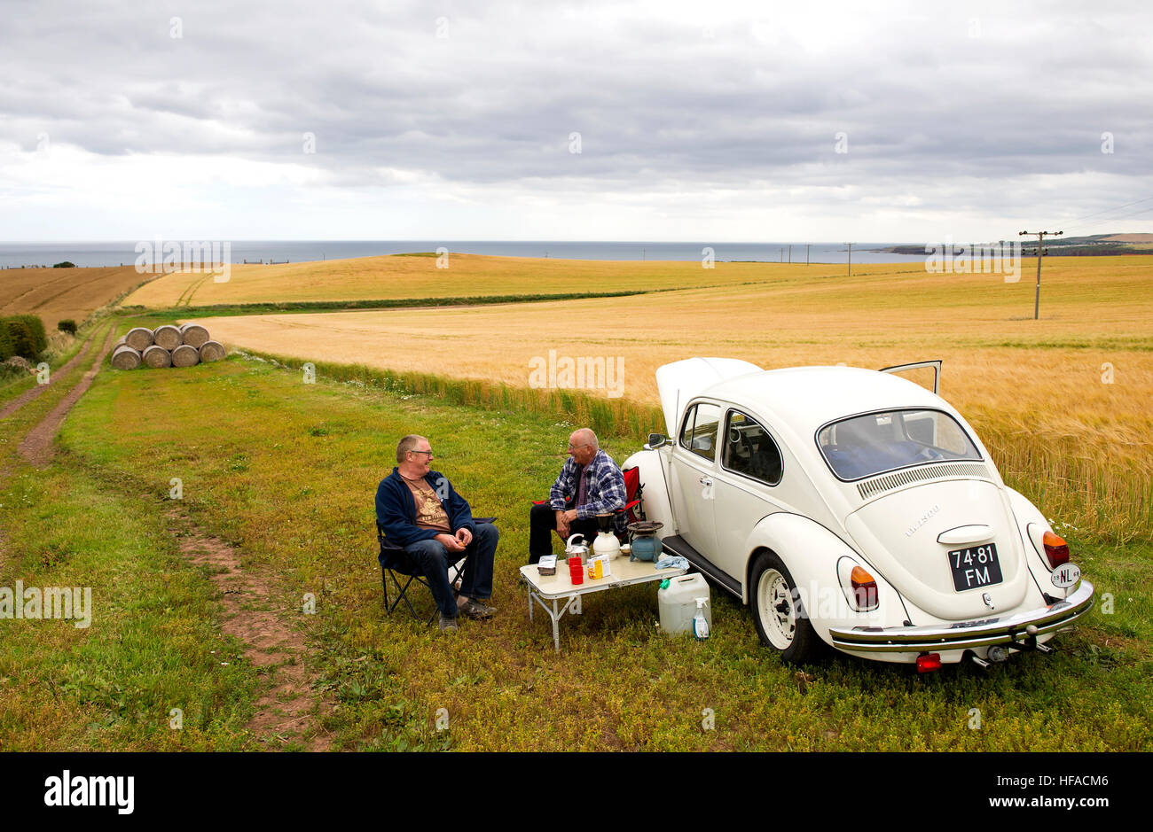 Two Dutch tourists have a picnic beside their VW beetle in a field near St Abbs, Berwickshire, Scottish Borders, Scotland, UK Stock Photo