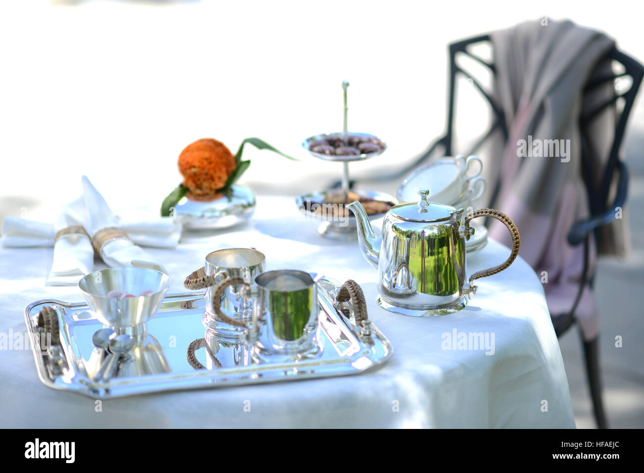 Table set for an English high tea, or afternoon tea, outside with silver teapot and linen